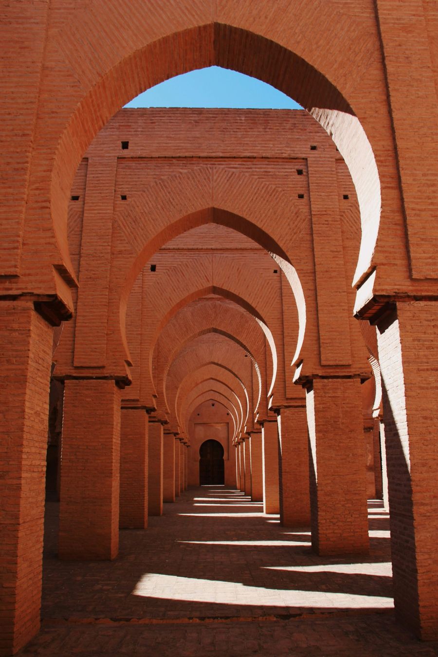 Row of repeating horseshoe arches in a red brick mosque corridor, Tin Mal, Morocco